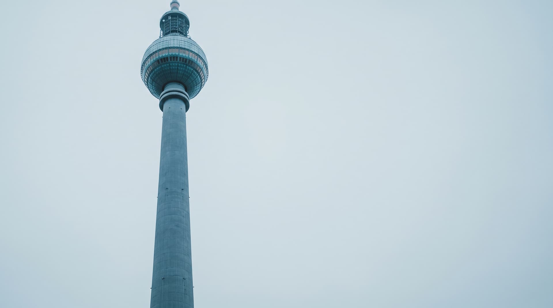Berliner Fernsehturm mit türkis schimmernder Kugel unter bedecktem Himmel, von unten fotografiert