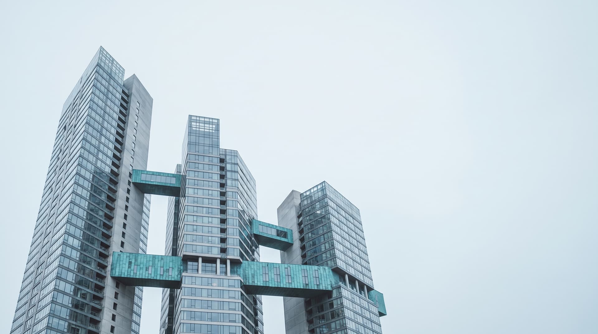 Several high-rise towers connected by bridges clad in patinated copper under an overcast sky