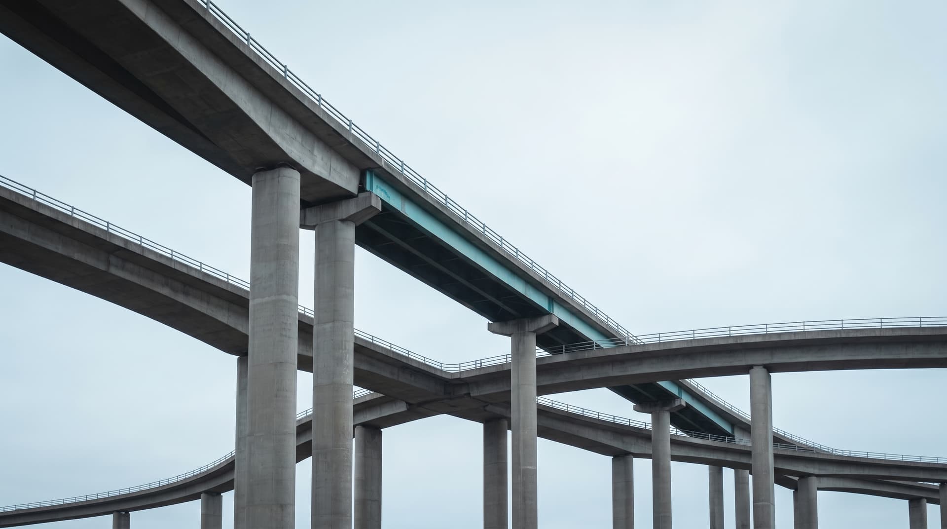 Intersecting concrete ramps of a motorway interchange with a teal-painted steel girder under an overcast sky – a metaphor for AI interfaces that connect systems