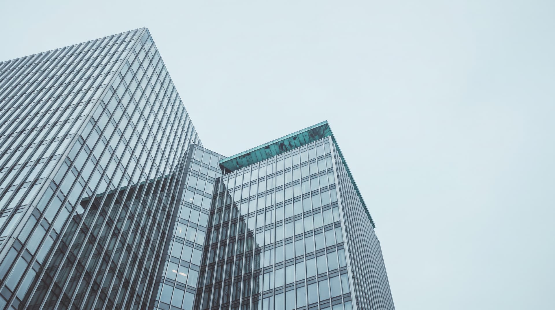 Glass high-rise facades in Berlin-Charlottenburg seen from below, with a verdigris copper roof edge against a pale grey sky