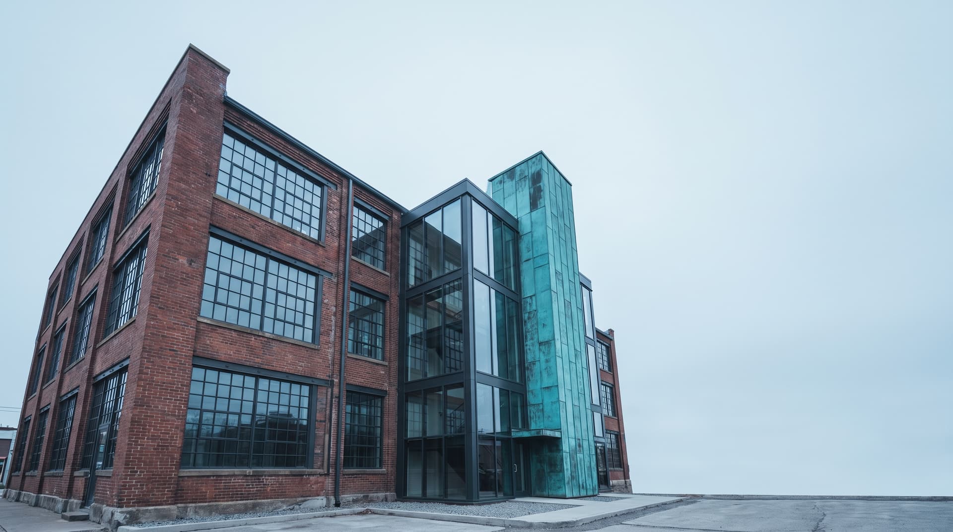 Umgebaute Backstein-Fabriketage mit gläsernem Anbau und grün patiniertem Kupfer-Treppenturm unter bedecktem Himmel – Sinnbild für KI-Startups