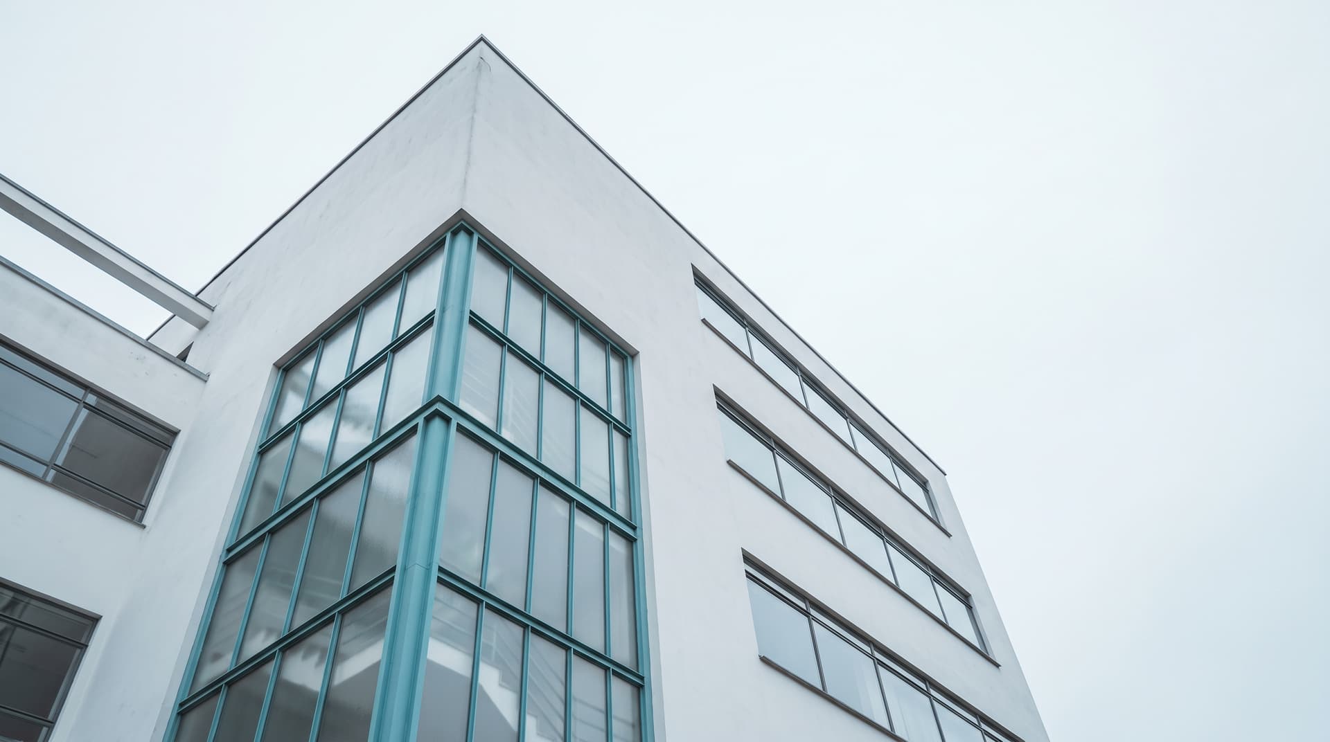White Bauhaus-style building with ribbon windows photographed from below, glazed staircase tower with teal steel frames
