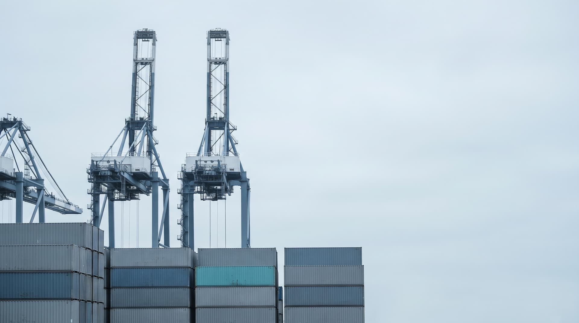 Gru portacontainer sopra container impilati in un porto, un container turchese, sotto un cielo coperto