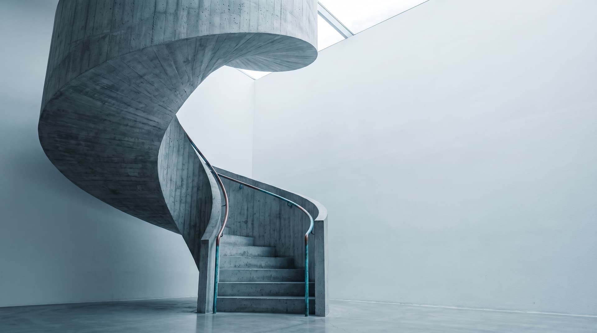Geschwungene Wendeltreppe aus Sichtbeton mit patiniertem Kupfergeländer, von unten fotografiert
