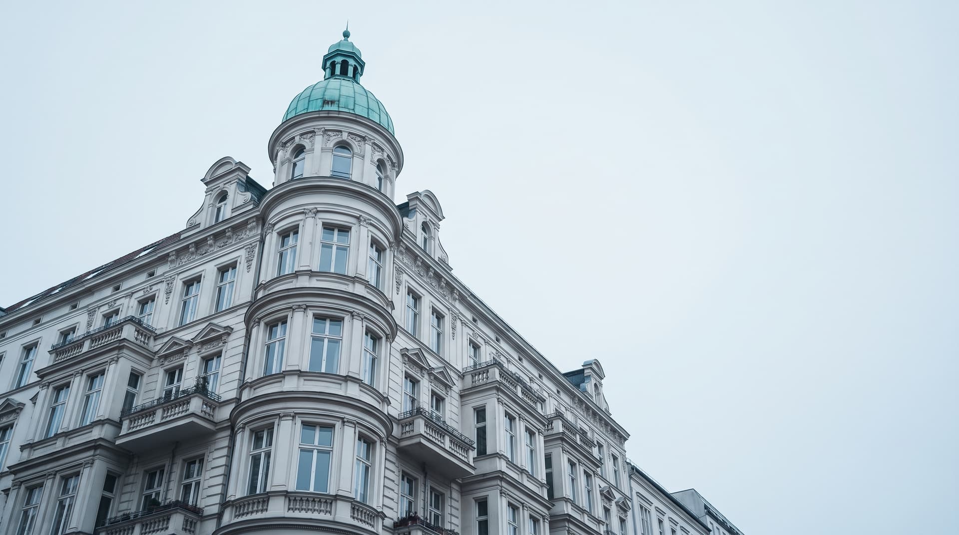 Gründerzeit-Eckhaus in Berlin-Charlottenburg von unten fotografiert, Eckturm mit grün patinierter Kupferkuppel vor hellem Himmel