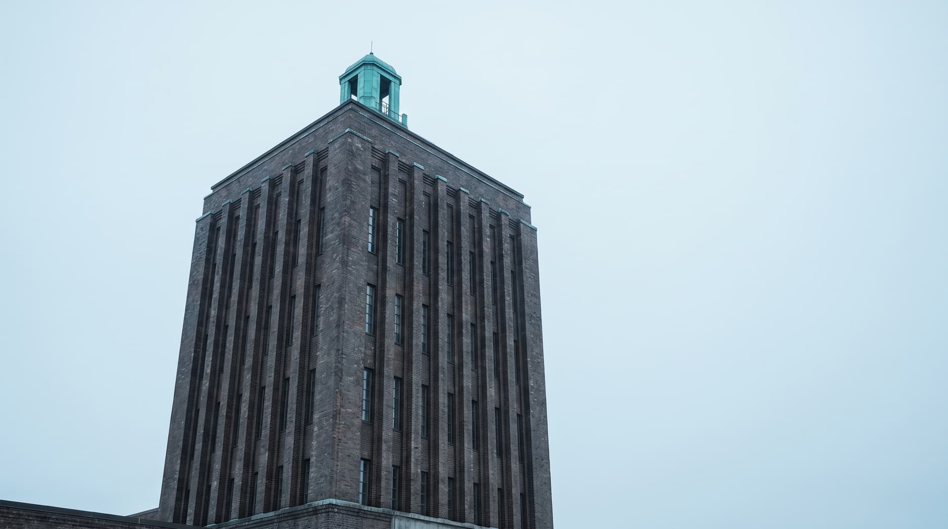 Expressionistischer Backsteinturm eines Zeitungshauses mit kupfergrüner Dachlaterne unter bedecktem Himmel – Sinnbild für Content-Produktion mit KI