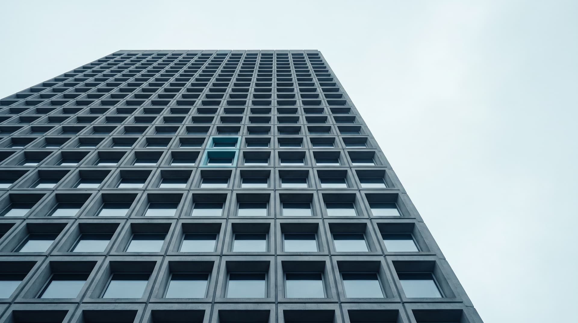 High-rise with a regular concrete grid facade photographed from below, a single window with a teal frame