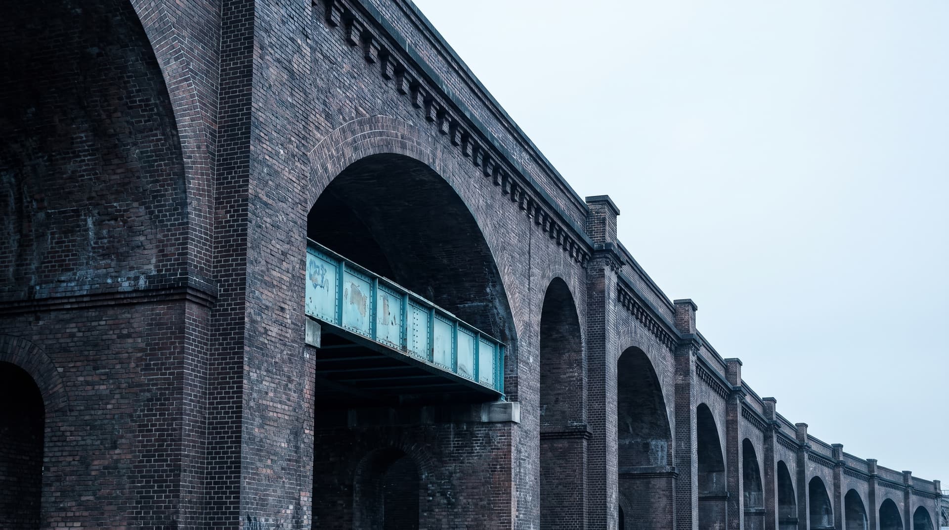 Berliner Backstein-Viadukt mit einer Reihe von Bögen von unten fotografiert, ein Stahlträger in Teal als Farbakzent