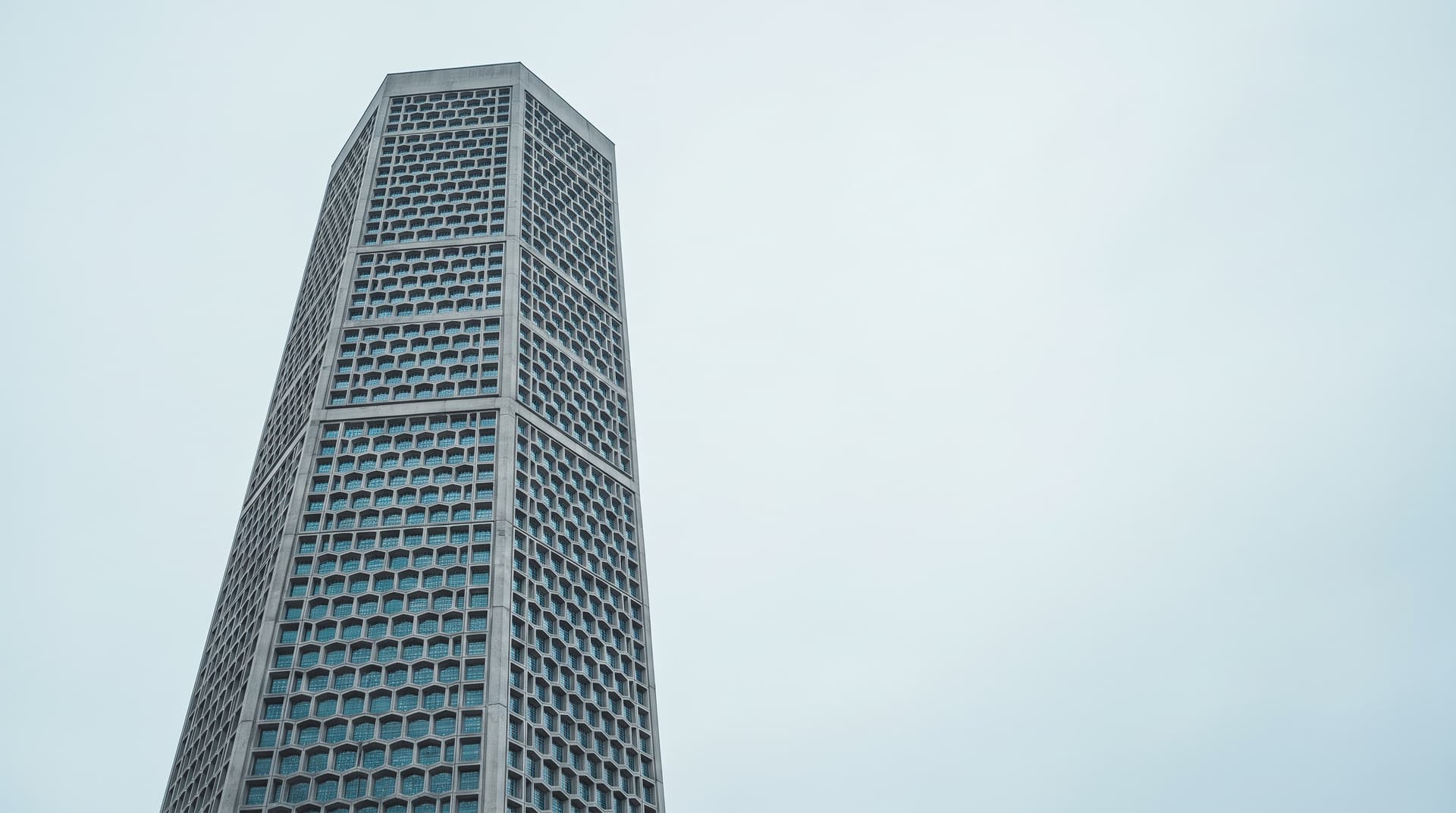 Octagonal tower with a honeycomb facade of glass blocks photographed from below, glass in muted teal blue against a pale sky