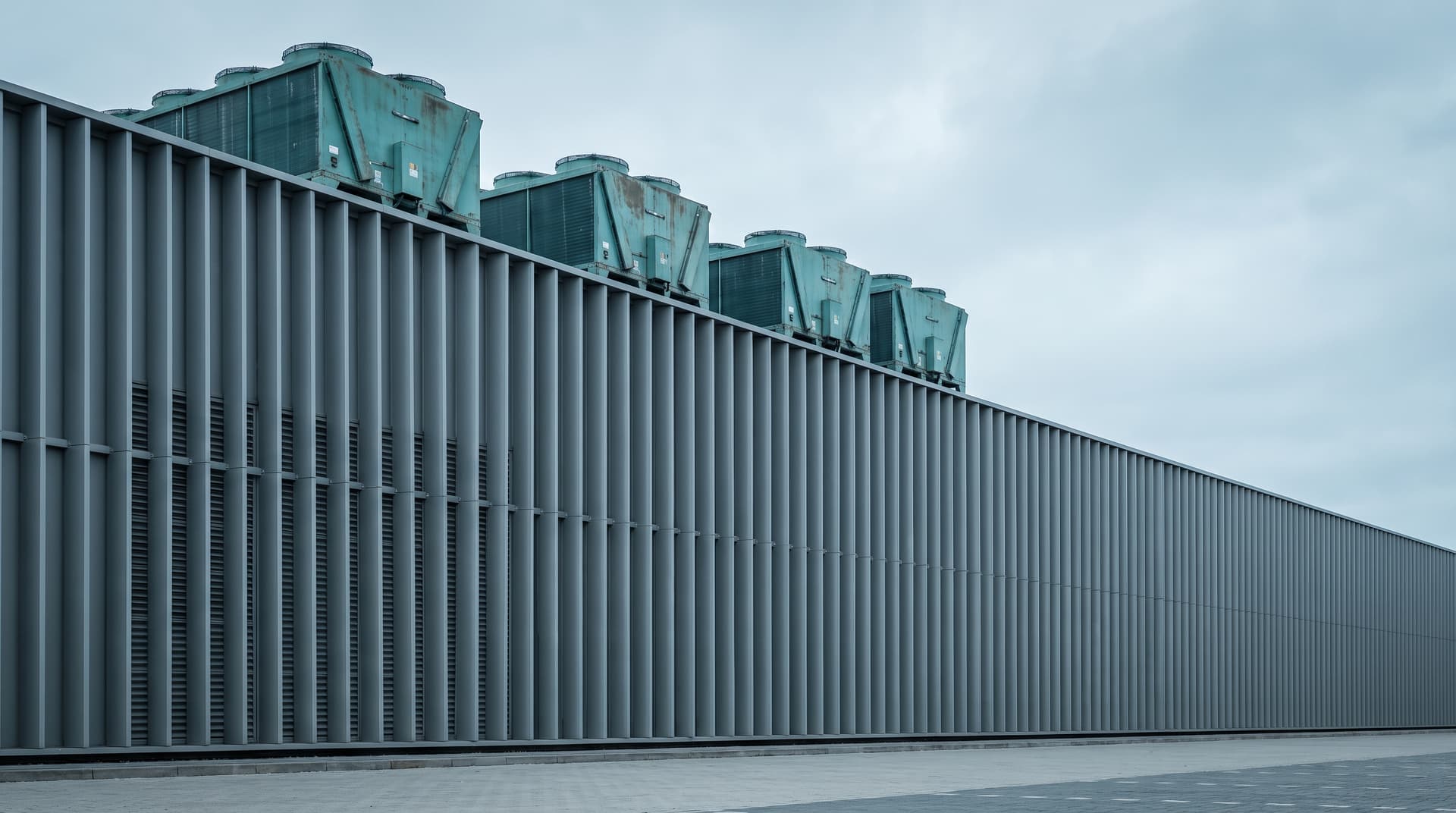 Data centre with a louvred facade and verdigris teal cooling units on the roof under an overcast sky – a visual metaphor for SaaS platforms with AI