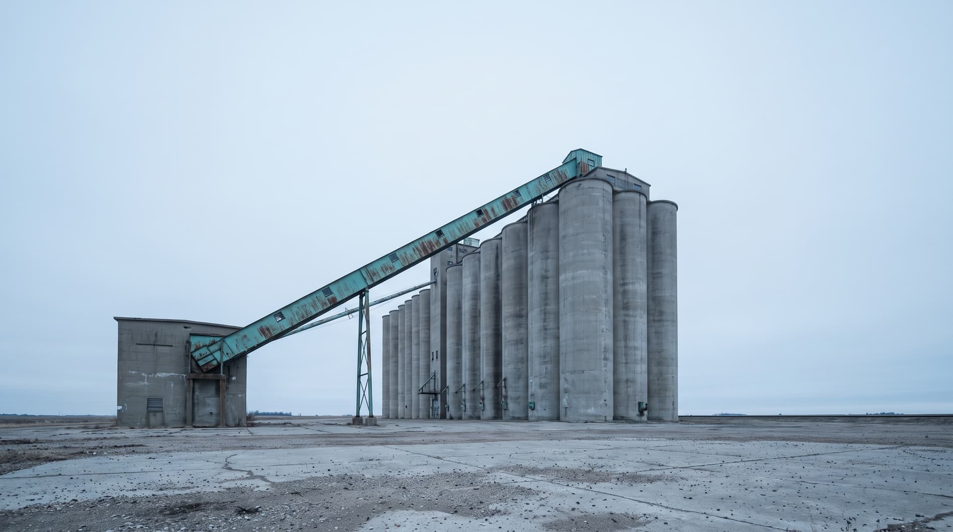 Betonsilos mit teal gestrichener Förderbandbrücke unter bedecktem Himmel – Sinnbild für KI in der industriellen Produktion
