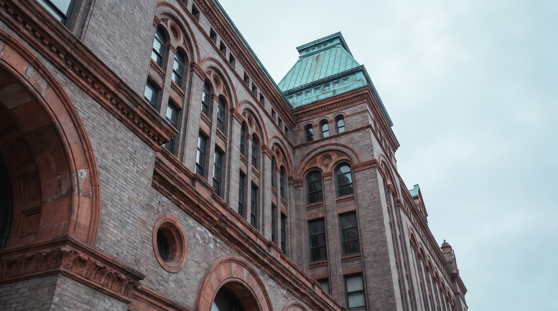 Historic brick post office building with long rows of windows photographed from below, corner roof of green patinated copper