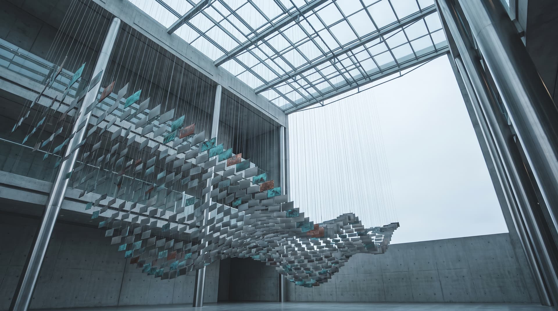 Schwebende Skulptur aus vielen Metallplatten unter dem Glasdach eines Atriums, von unten fotografiert