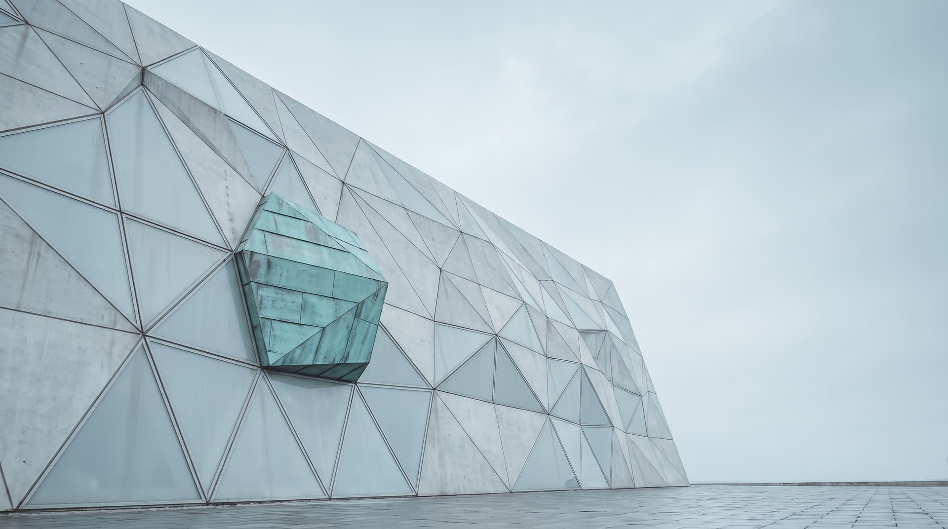 Parametrische Fassade aus hellen Dreieckspaneelen mit einem Feld aus grün patiniertem Kupfer unter bedecktem Himmel – Sinnbild für KI-native Softwarearchitektur