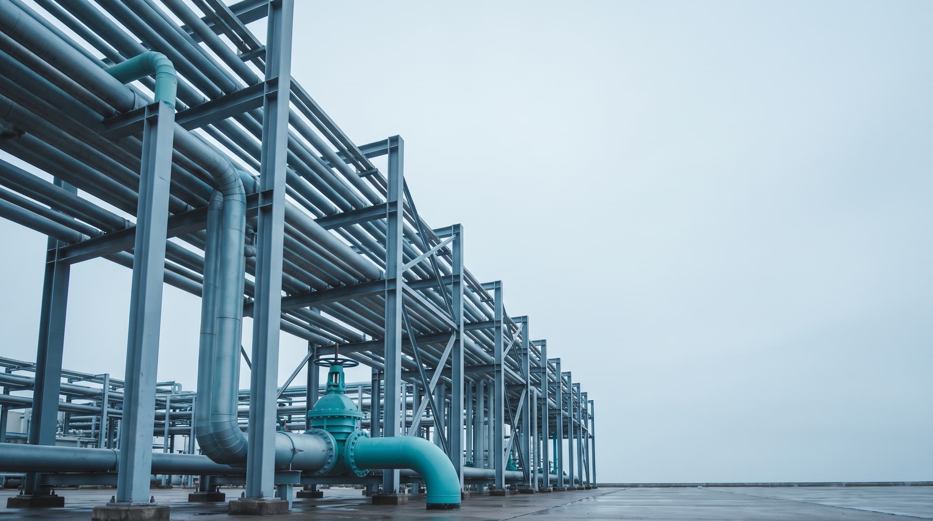 Steel pipe rack with parallel pipelines and a teal valve at an industrial plant, photographed from below