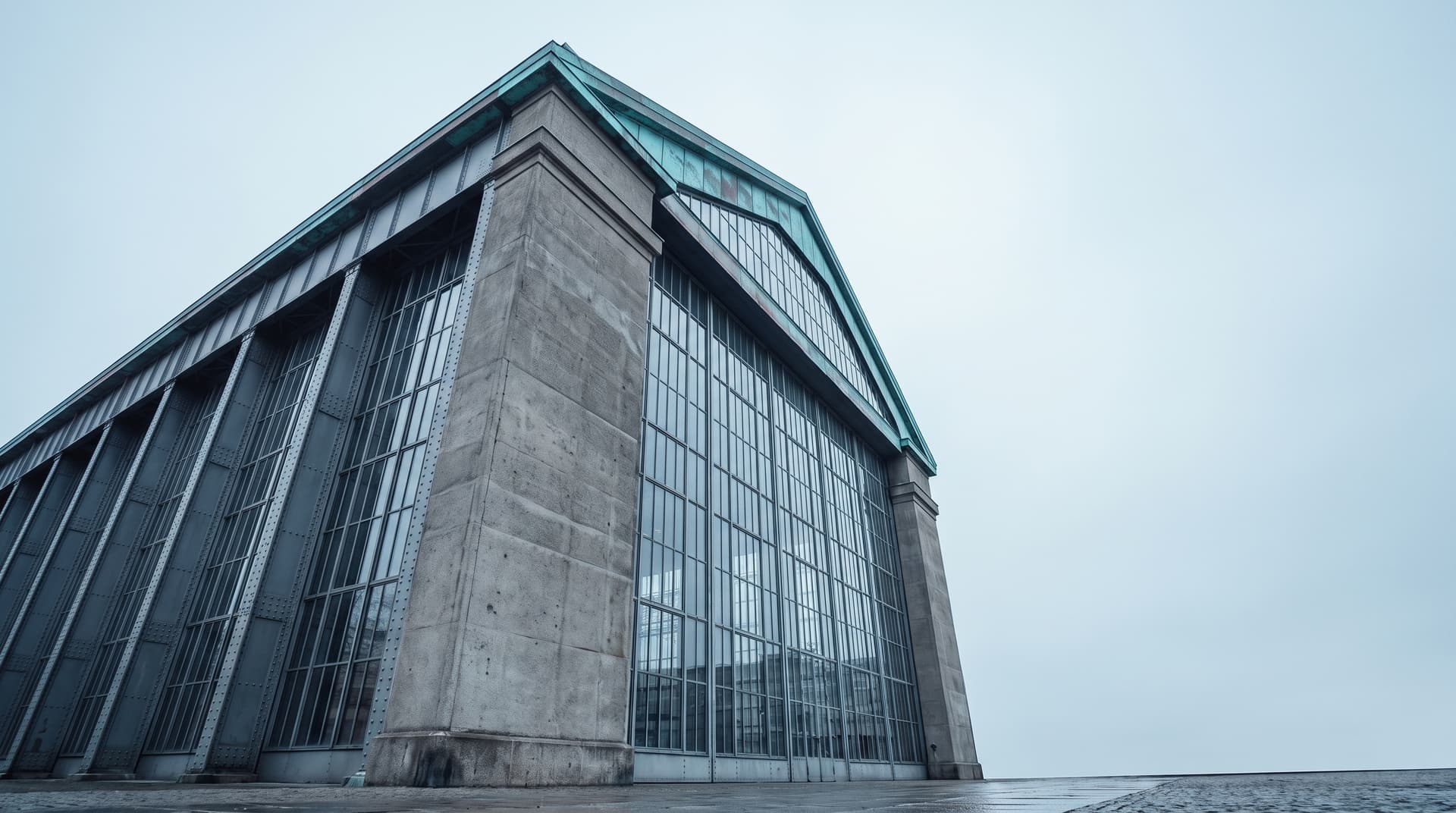 Monumentale capannone industriale in acciaio, vetro e cemento a Berlino visto dal basso, con un timpano in rame patinato verderame sotto un cielo coperto