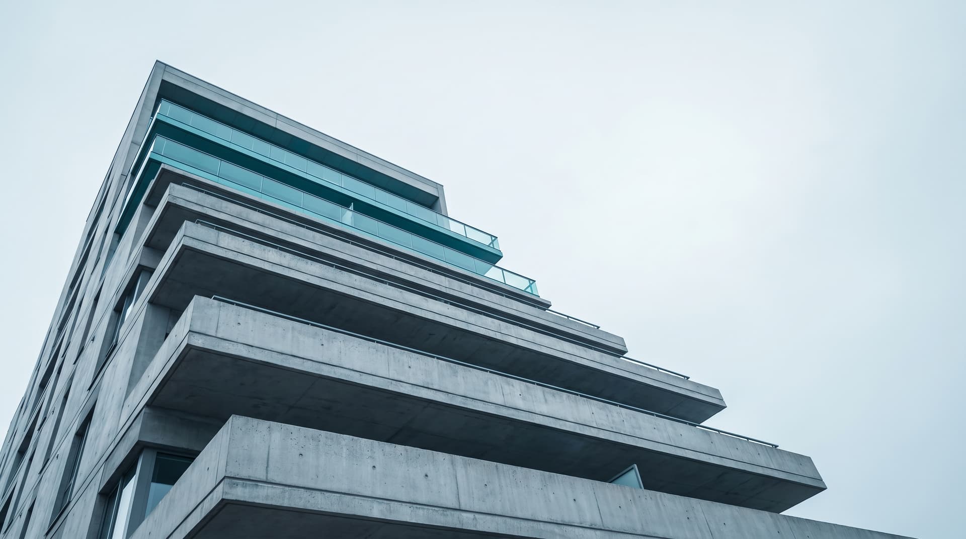 Gestaffelter Terrassenbau aus Beton von unten fotografiert, oberste Stufe mit Glasbrüstung in Teal