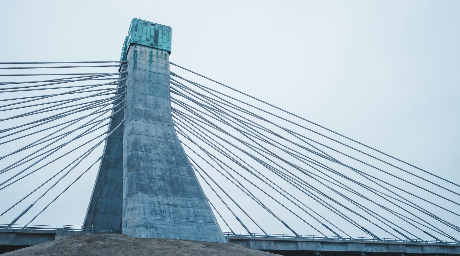 Betonpylon einer Schrägseilbrücke mit zusammenlaufenden Stahlseilen und grün patinierter Kupferkappe unter bedecktem Himmel – Sinnbild für die Anbindung von KI an bestehende Systeme